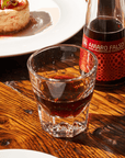 Amaro Falso non-alcoholic cocktail in a glass with a bottle of Amaro Falso on a wooden table.