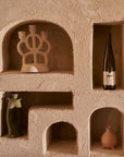 Wine bottle and decorative items in embedded shelves of a textured wall.