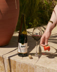 Bottle of wine, glass with red wine, and a strawberry on a stone surface outdoors.
