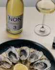Bottle of NON wine, glass of white wine, and plate of oysters on a table.