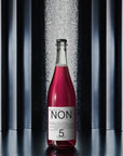 Bottle of red liquid with a white label against a black and gray striped background