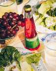 Table setting with a bottle of red beverage, grapes, and salad.