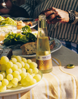 Table with grapes, bread, and a bottle of Phony White wine on a striped tablecloth.