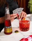 Person pouring a Phony Espresso Negroni from a bottle into a glass with playing cards on a table.