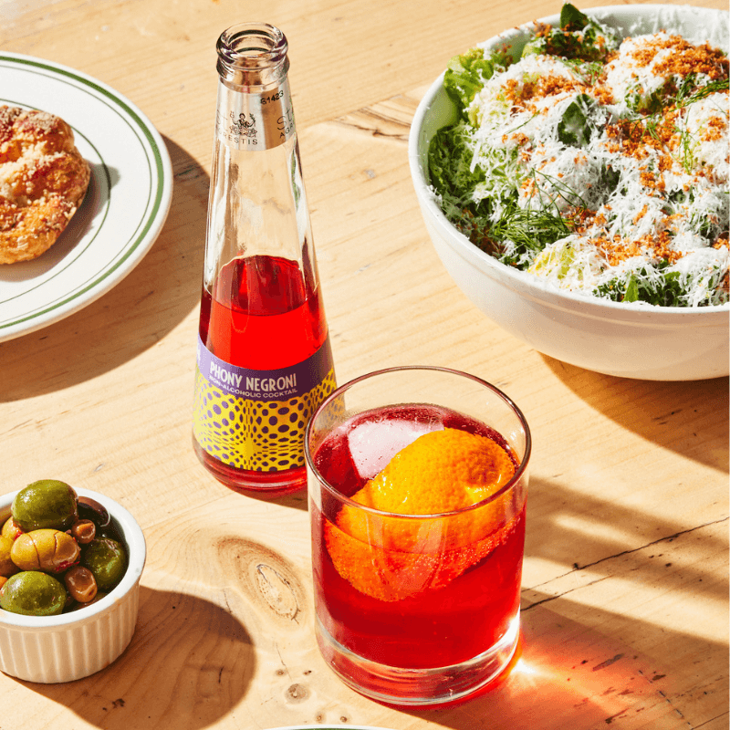 Phony Negroni bottle with a glass on a wooden table with food.