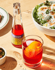 Phony Negroni bottle with a glass on a wooden table with food.