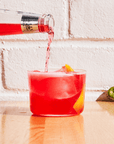 Phony Negroni being poured into a glass with ice and a bottle cap on a wooden surface.