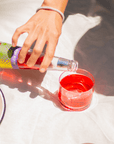Hand pouring phony negroni from a colorful bottle into a glass on a white surface.