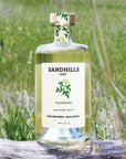 Bottle of Sandhills Elixir on a wooden log with a grassy field background