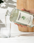 Person pouring liquid from a 'Sandhills' bottle into a glass with ice on a light background.