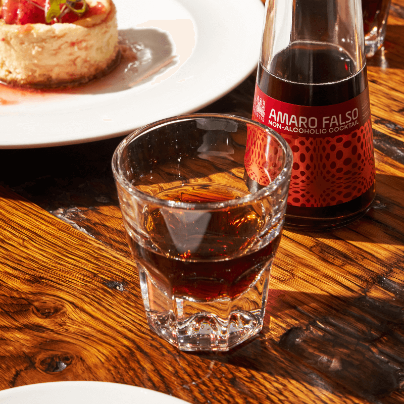 Amaro Falso non-alcoholic cocktail in a glass with a bottle of Amaro Falso on a wooden table.