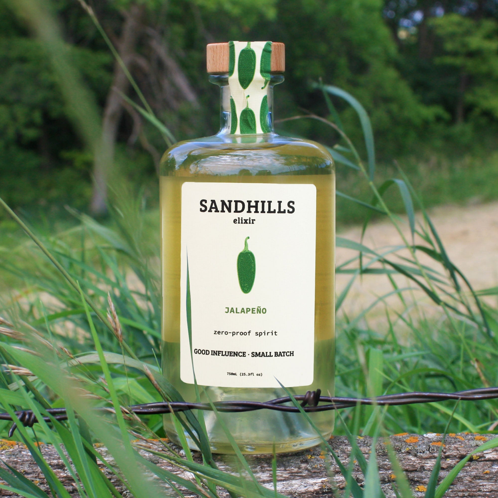 Bottle of Sandhills elixir jalapeño spirit with a green label in a natural setting.
