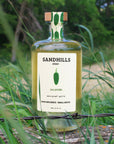 Bottle of Sandhills elixir jalapeño spirit with a green label in a natural setting.