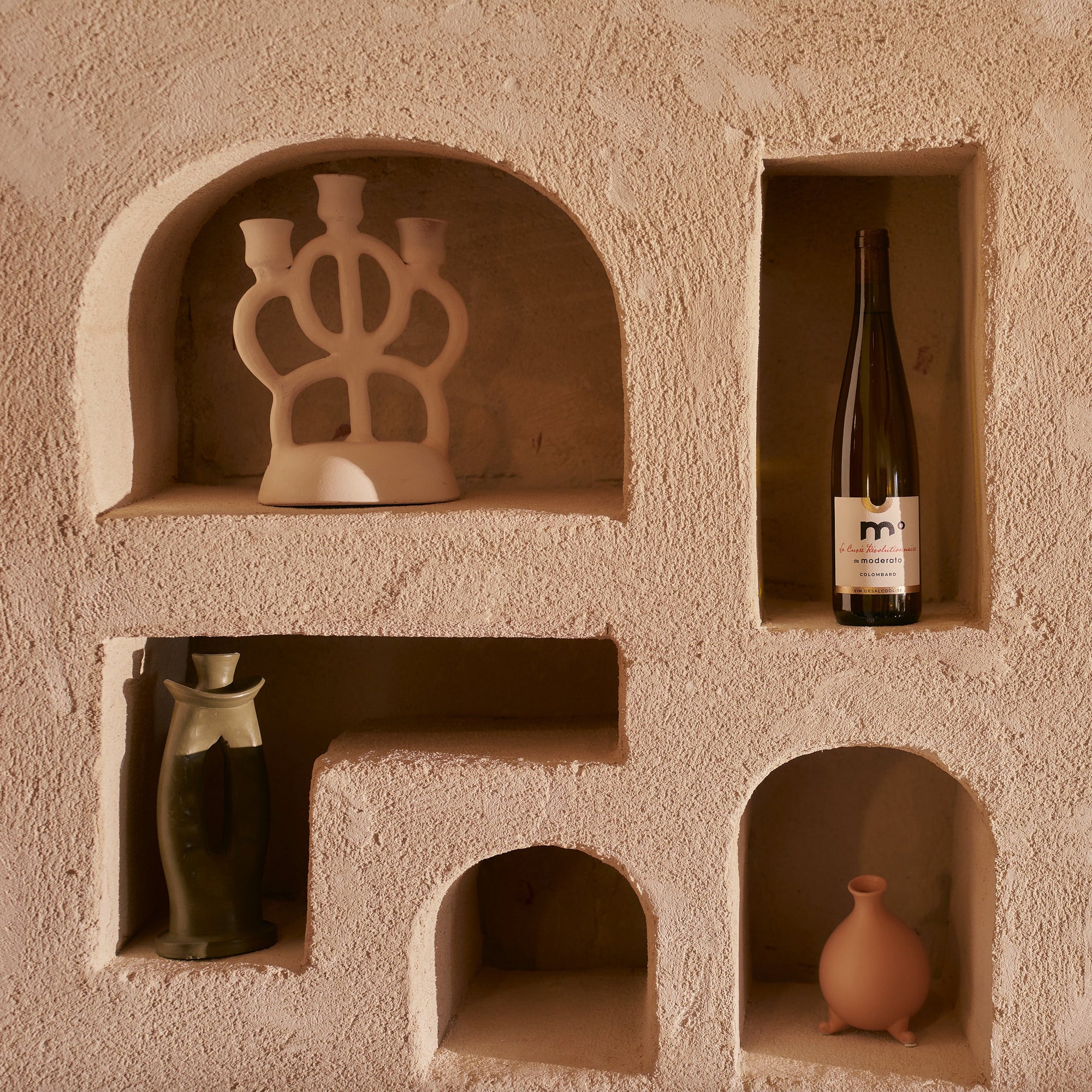 Wine bottle and decorative items in embedded shelves of a textured wall.