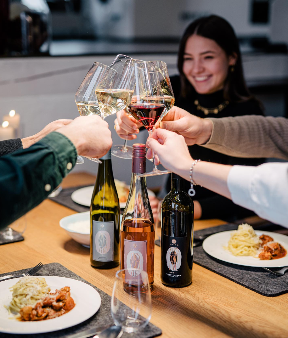 a group cheers at dinner with three different bottles of wine; white, rose, and red. 