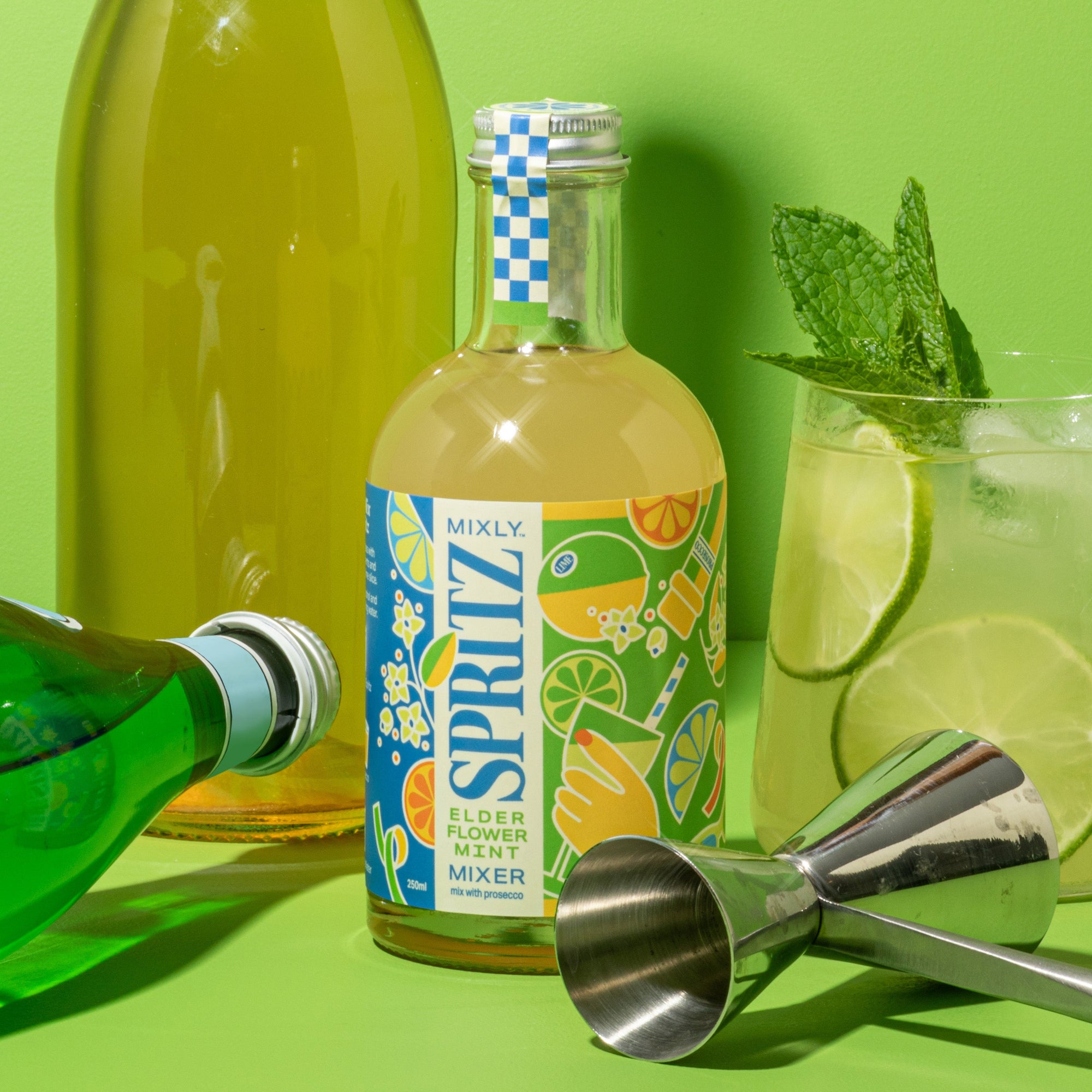 Bottle of Mixly Spritz elderflower mint mixer with a cocktail glass and lime garnish on a green background
