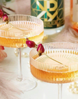 Two cocktail glasses with a floral garnish on a decorative table.