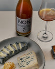 Bottle of Non alcoholic wine, glass with drink, and plate of cheese on a table