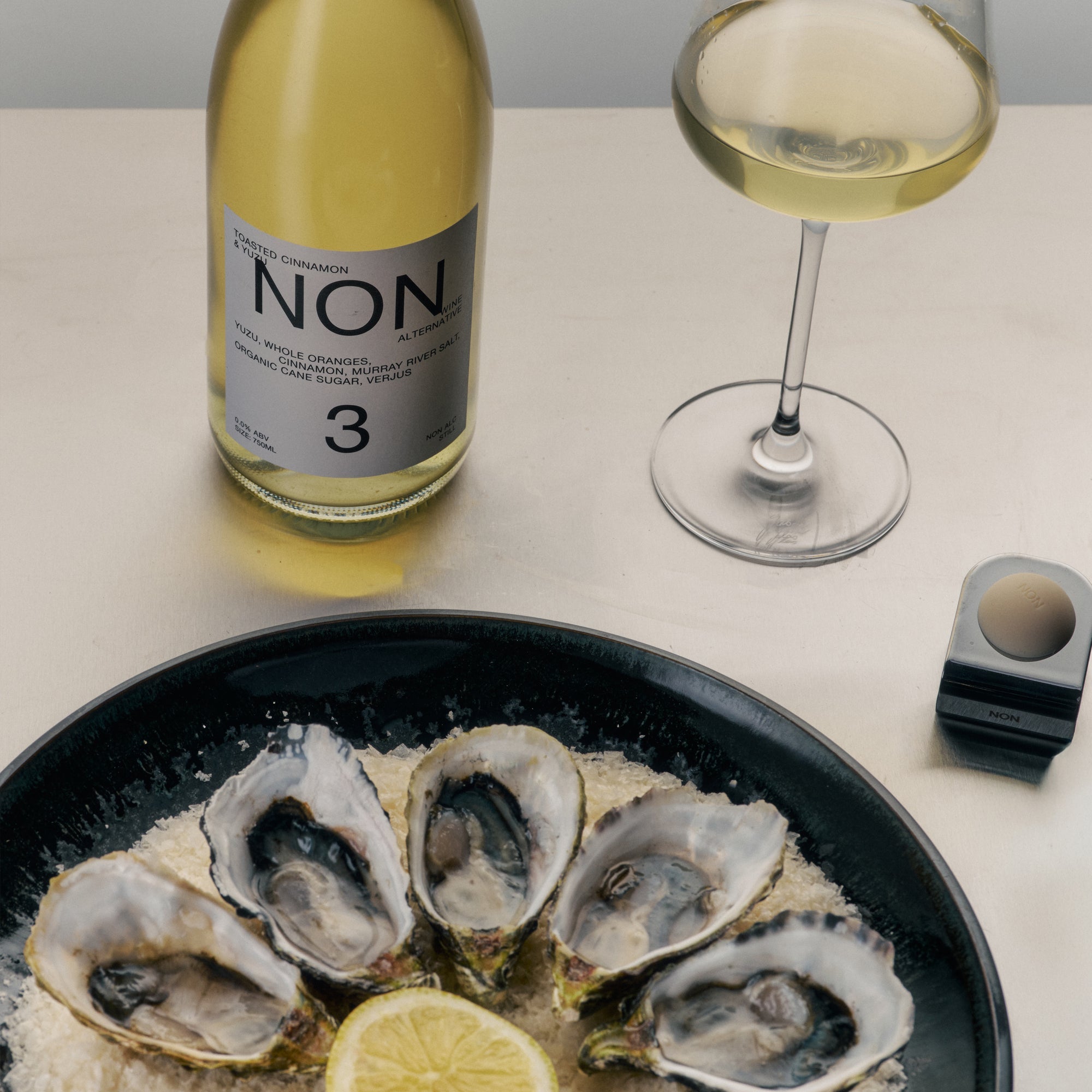 Bottle of NON wine, glass of white wine, and plate of oysters on a table.