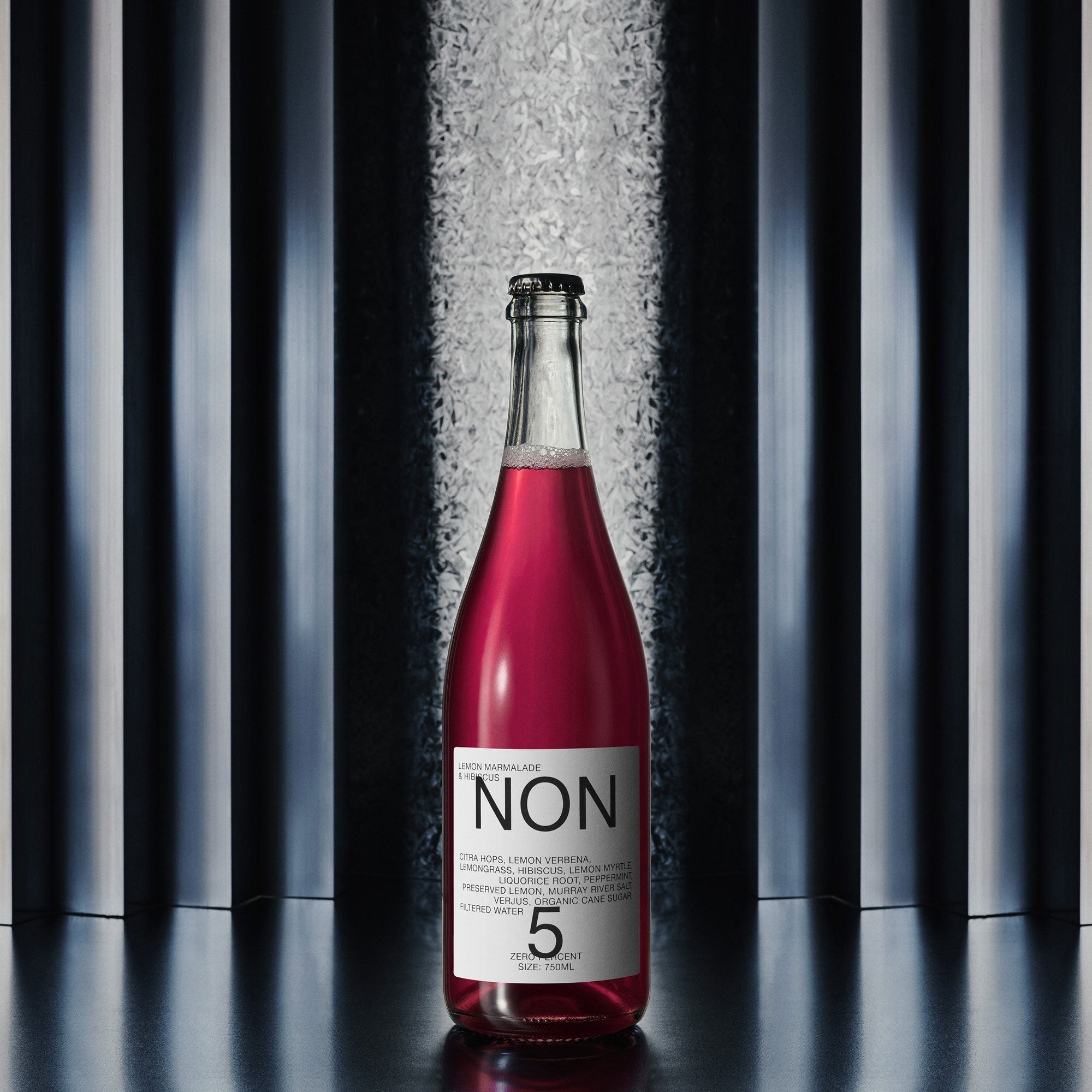 Bottle of red liquid with a white label against a black and gray striped background