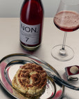 Bottle of NON 7 wine, glass of red wine, and cinnamon roll on a tray.