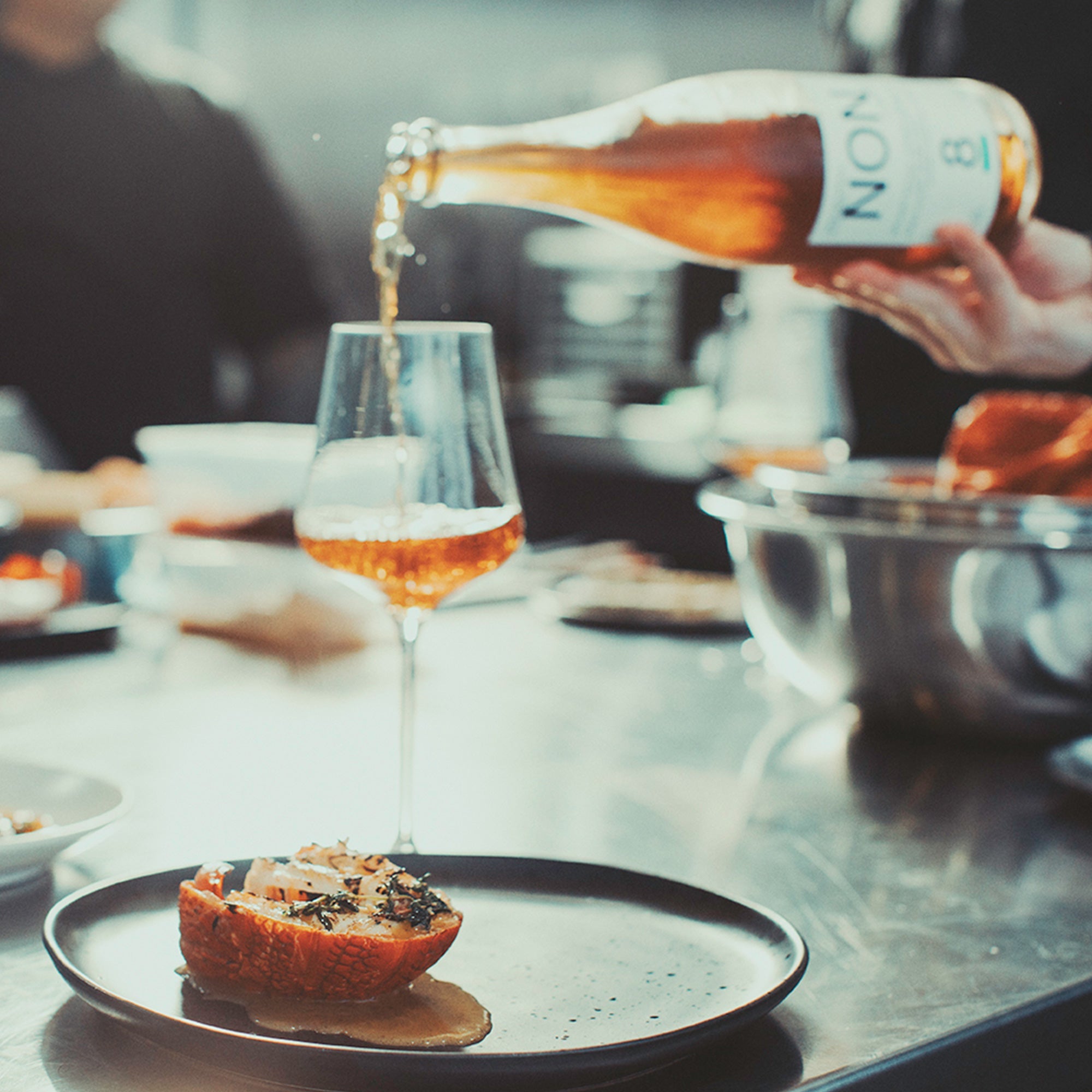 Person pouring a drink from a bottle into a glass on a table with food.