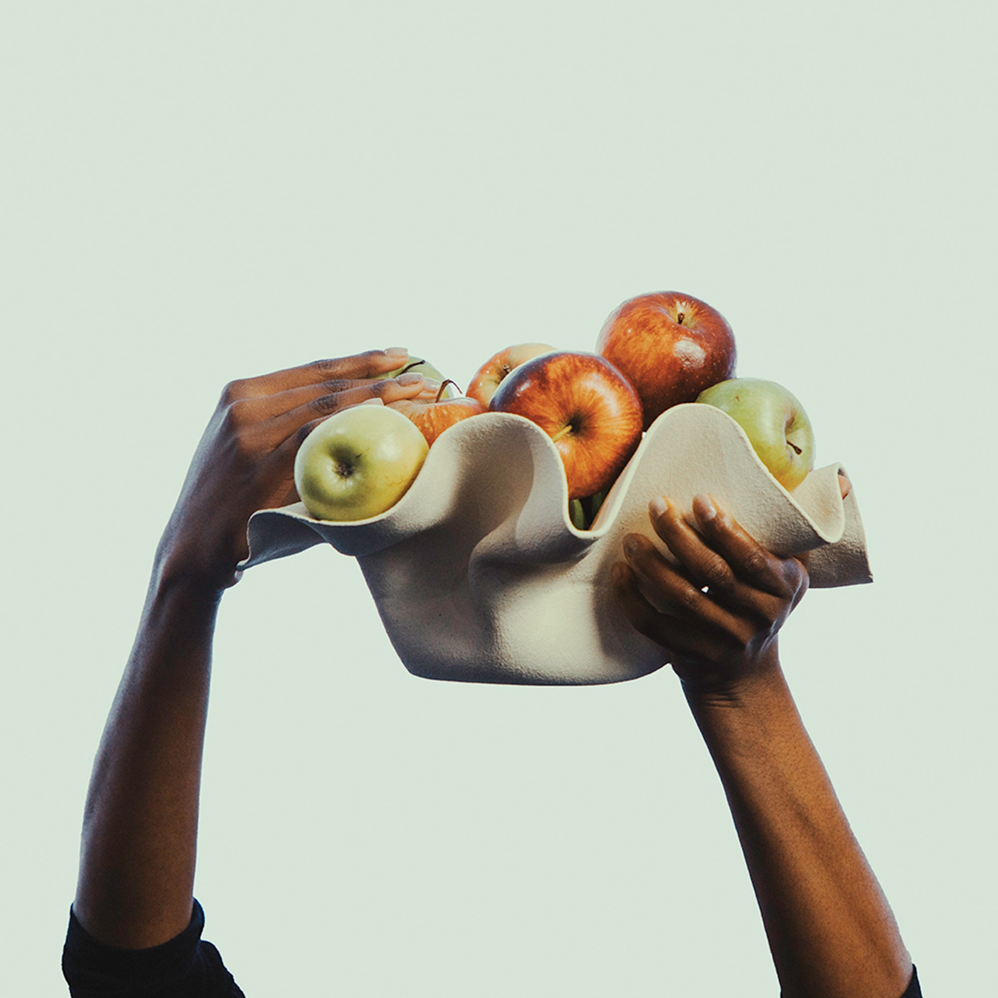 Two hands holding a ceramic bowl filled with apples against a light background