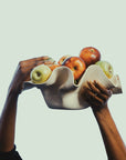 Two hands holding a ceramic bowl filled with apples against a light background