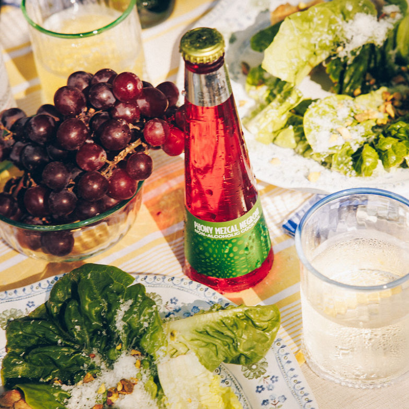 Table setting with a bottle of red beverage, grapes, and salad.