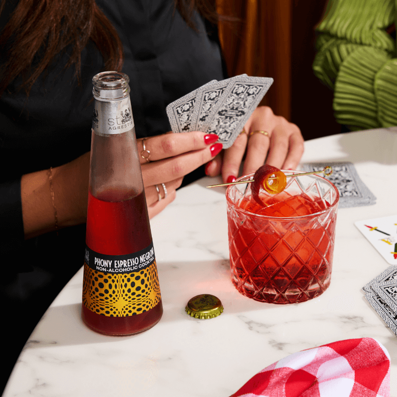 Person pouring a Phony Espresso Negroni from a bottle into a glass with playing cards on a table.