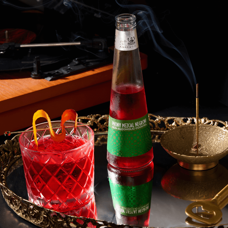 Bottle of Phony Mezcal Negroni with a cocktail on a reflective surface, record player in the background