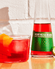 Non-alcoholic cocktail in a glass with a bottle of 'Phony Mezcal Negroni' on a light brick background