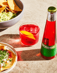 Phony Mezcal Negroni in a glass and a bottle on a concrete surface with Mexican food.