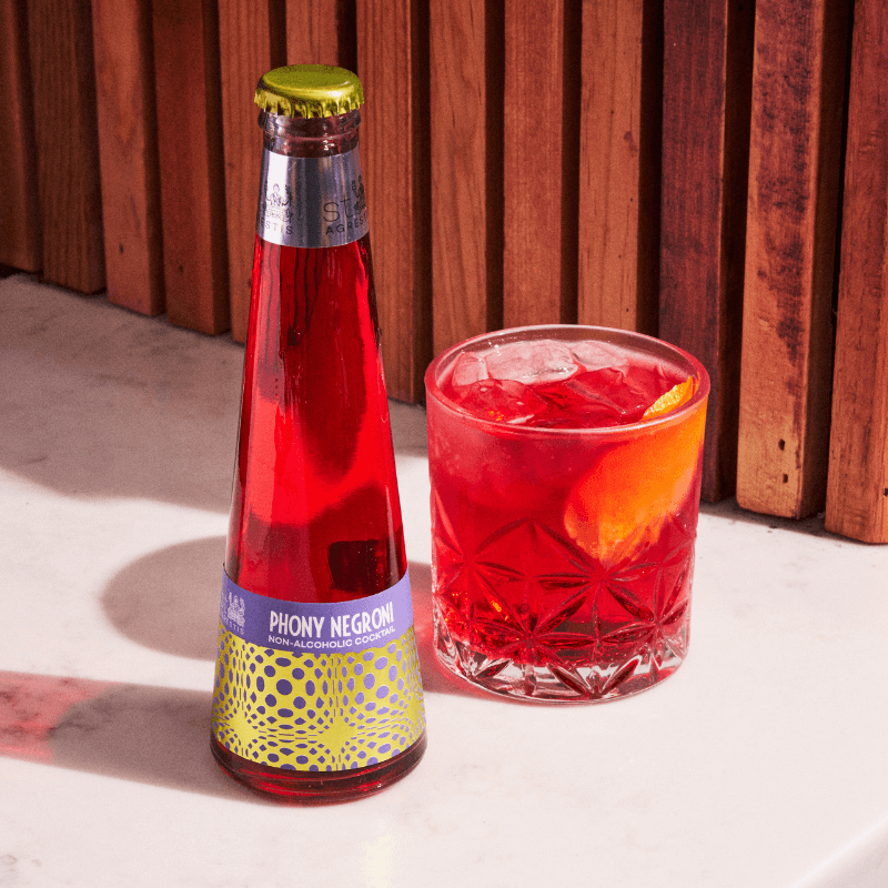 Bottle and glass of Phony Negroni against a wooden background
