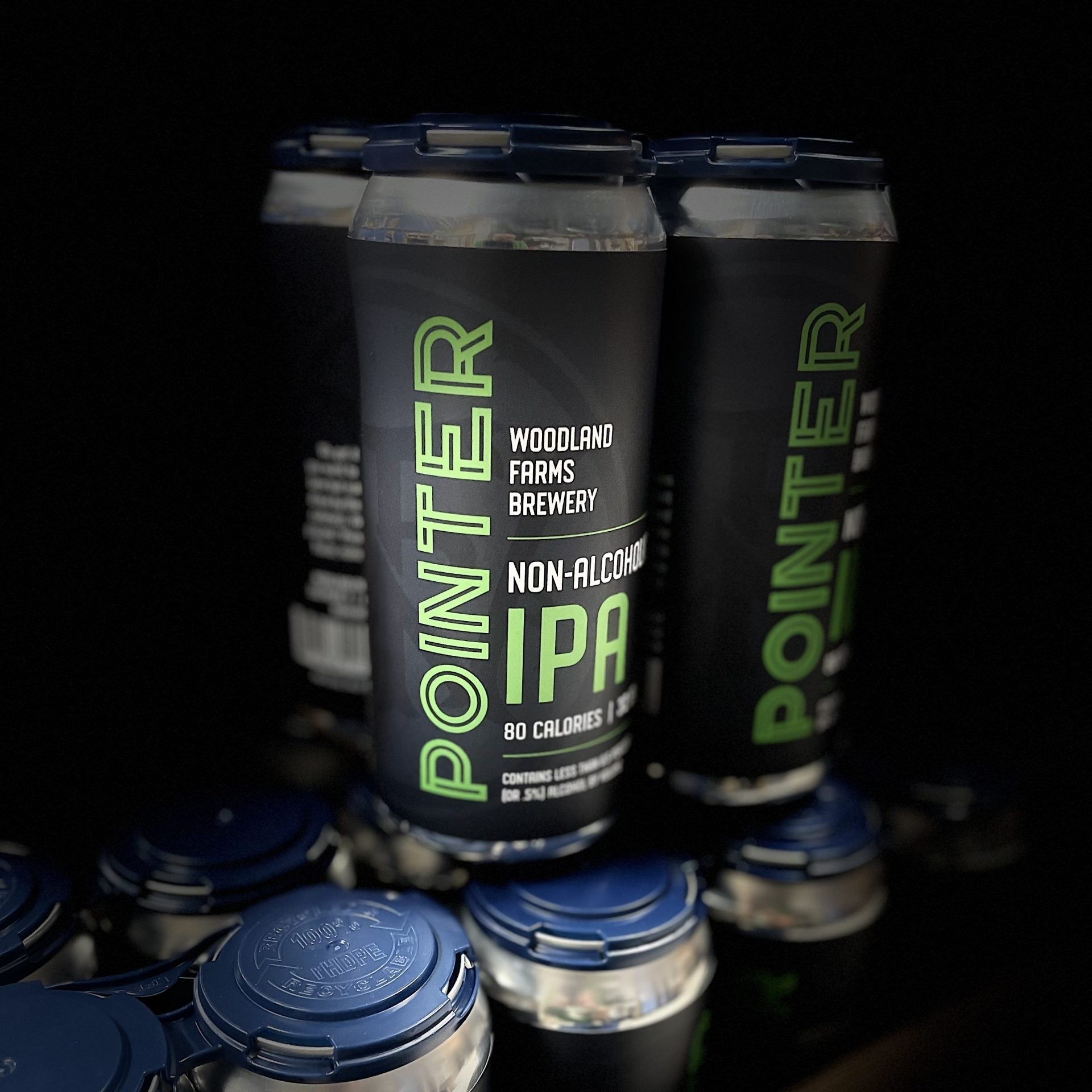 Multiple cans of Pointer Non-Alcoholic IPA with blue lids on a dark background