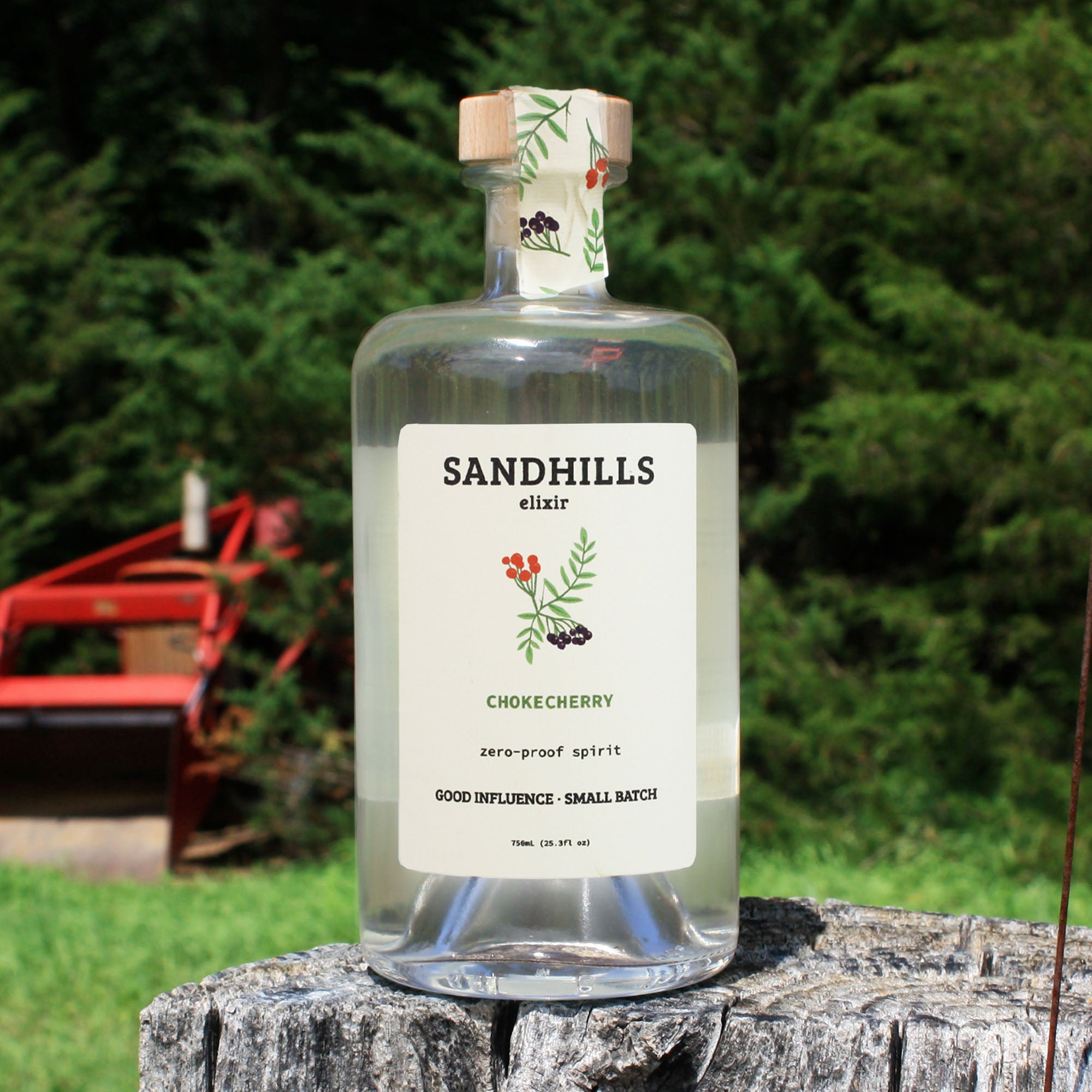 Bottle of Sandhills Elixir Chokecherry zero-proof spirit on a wooden log with a blurred green background