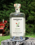 Bottle of Sandhills Elixir Chokecherry zero-proof spirit on a wooden log with a blurred green background