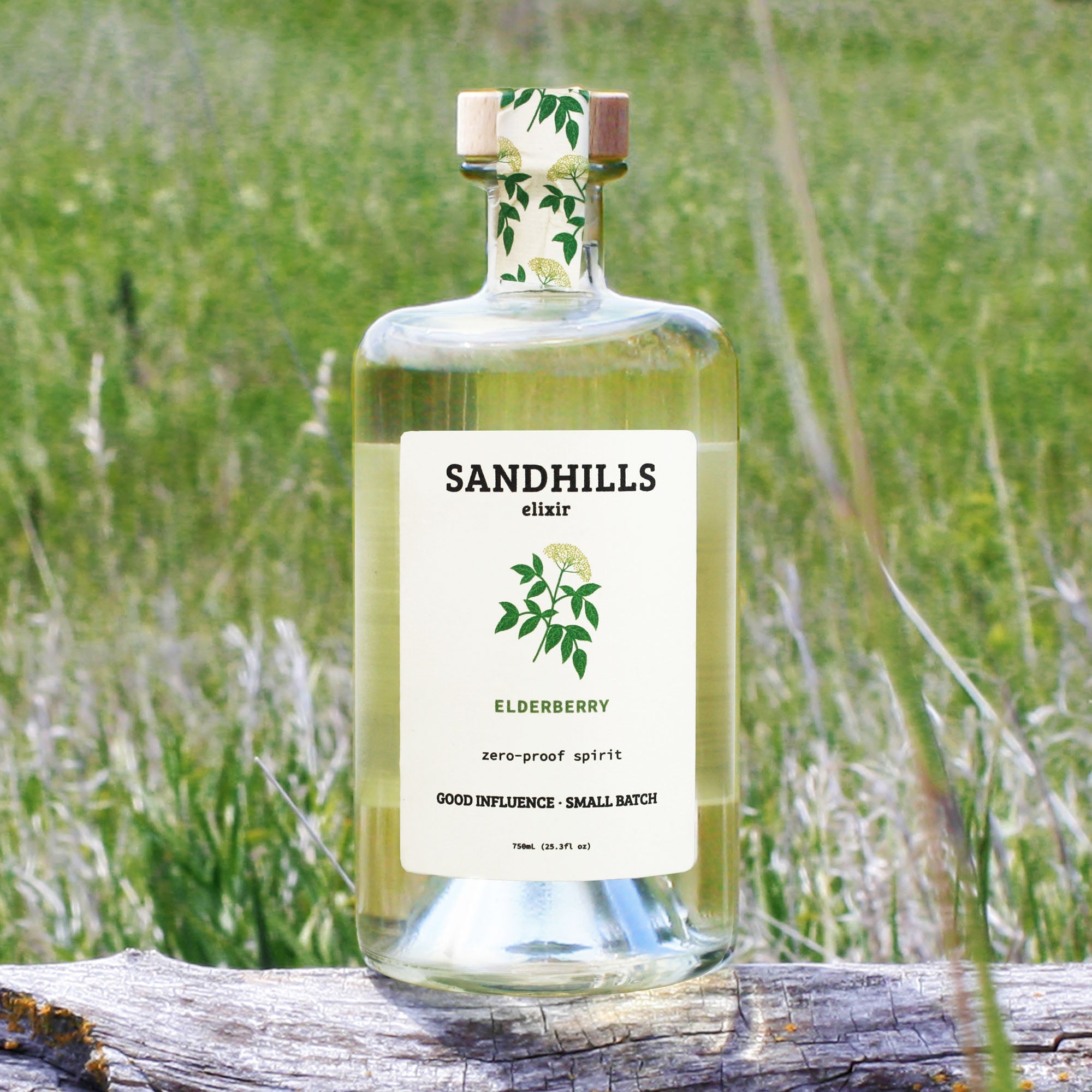 Bottle of Sandhills Elixir on a wooden log with a grassy field background