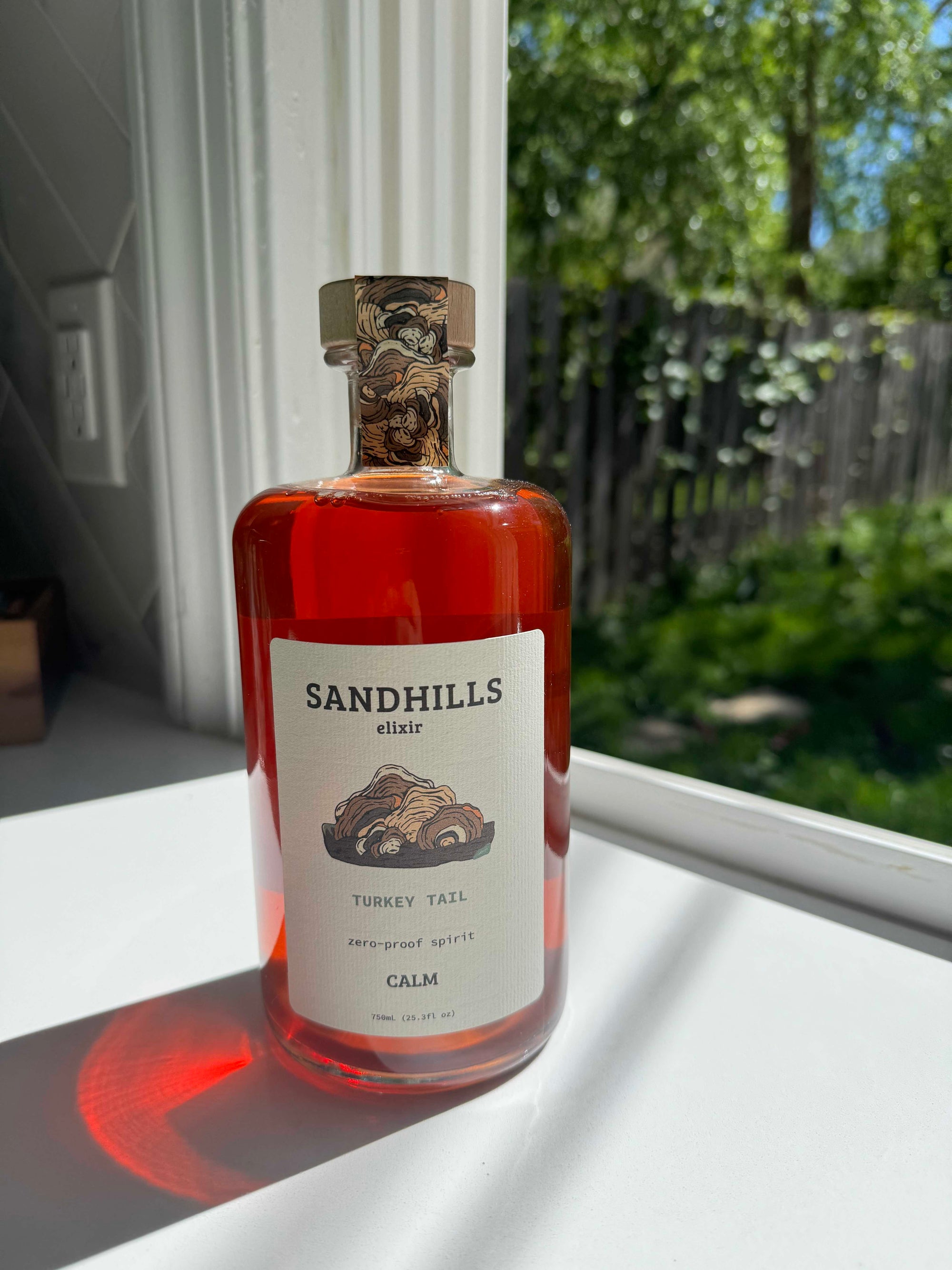 Bottle of Sandhills elixir on a windowsill with a garden view