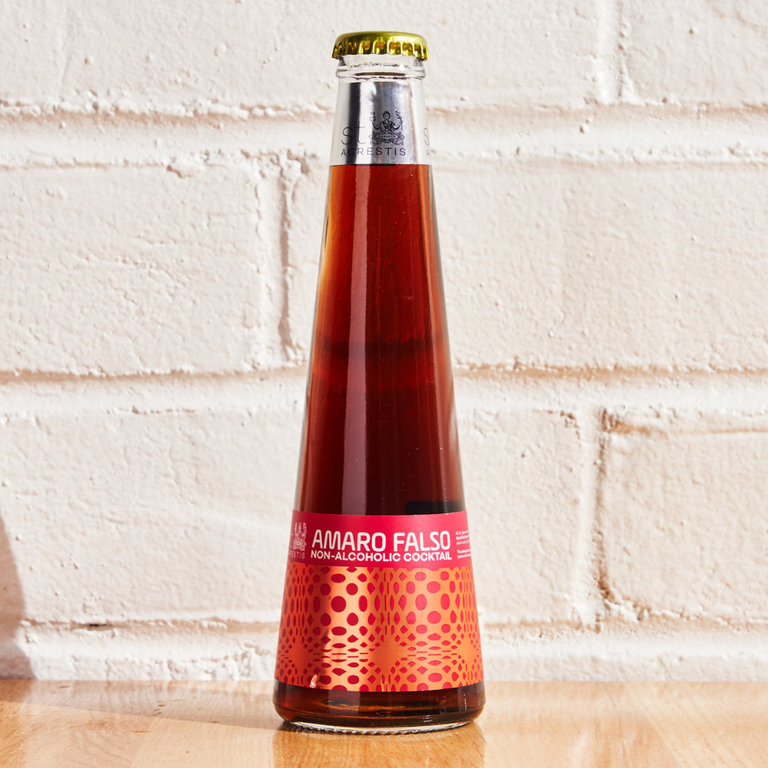 Bottle of Amaro Falso non-alcoholic cocktail on a wooden surface with a white brick wall background