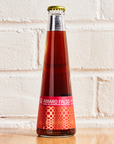 Bottle of Amaro Falso non-alcoholic cocktail on a wooden surface with a white brick wall background