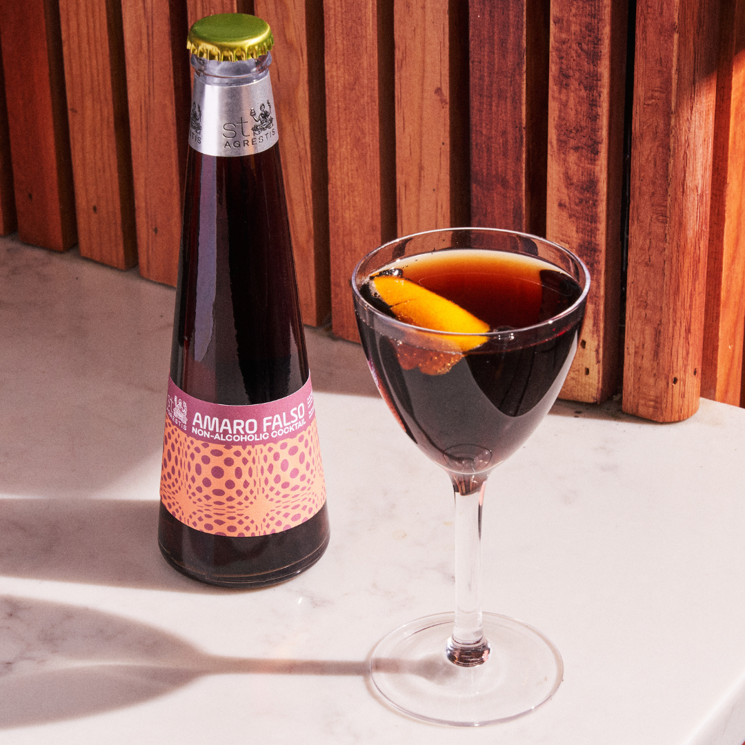 Bottle of Amaro Falso with a glass of dark liquid on a wooden surface