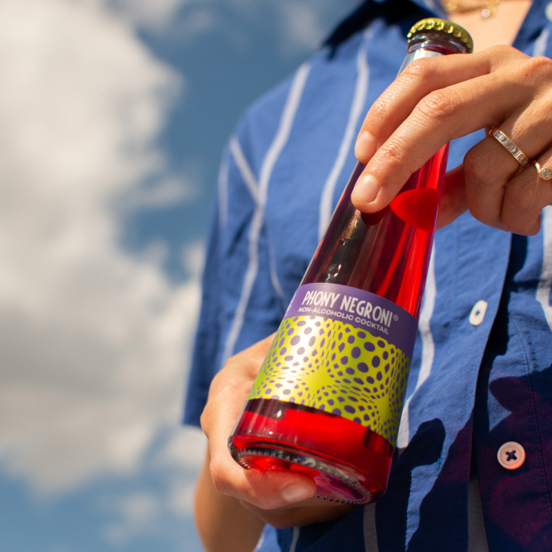 Person holding a bottle of Phony Negroni against a blue sky.