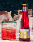 Bottle and glass of red cocktail with 'Phony Negroni' label on a blurred outdoor background