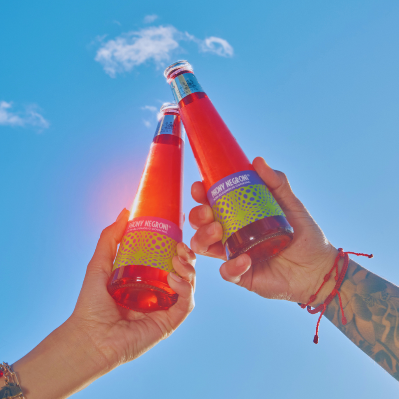 Two hands holding red bottles against a blue sky