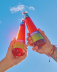 Two hands holding red bottles against a blue sky
