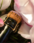 Bottle of champagne with a cork labeled 'CLIN' amidst pink flowers