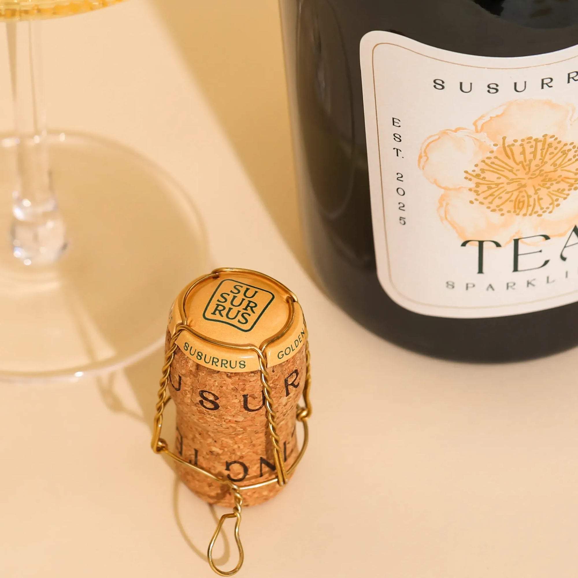 Bottle of Susurrus Tea Sparkling Wine with cork and glass on a light surface