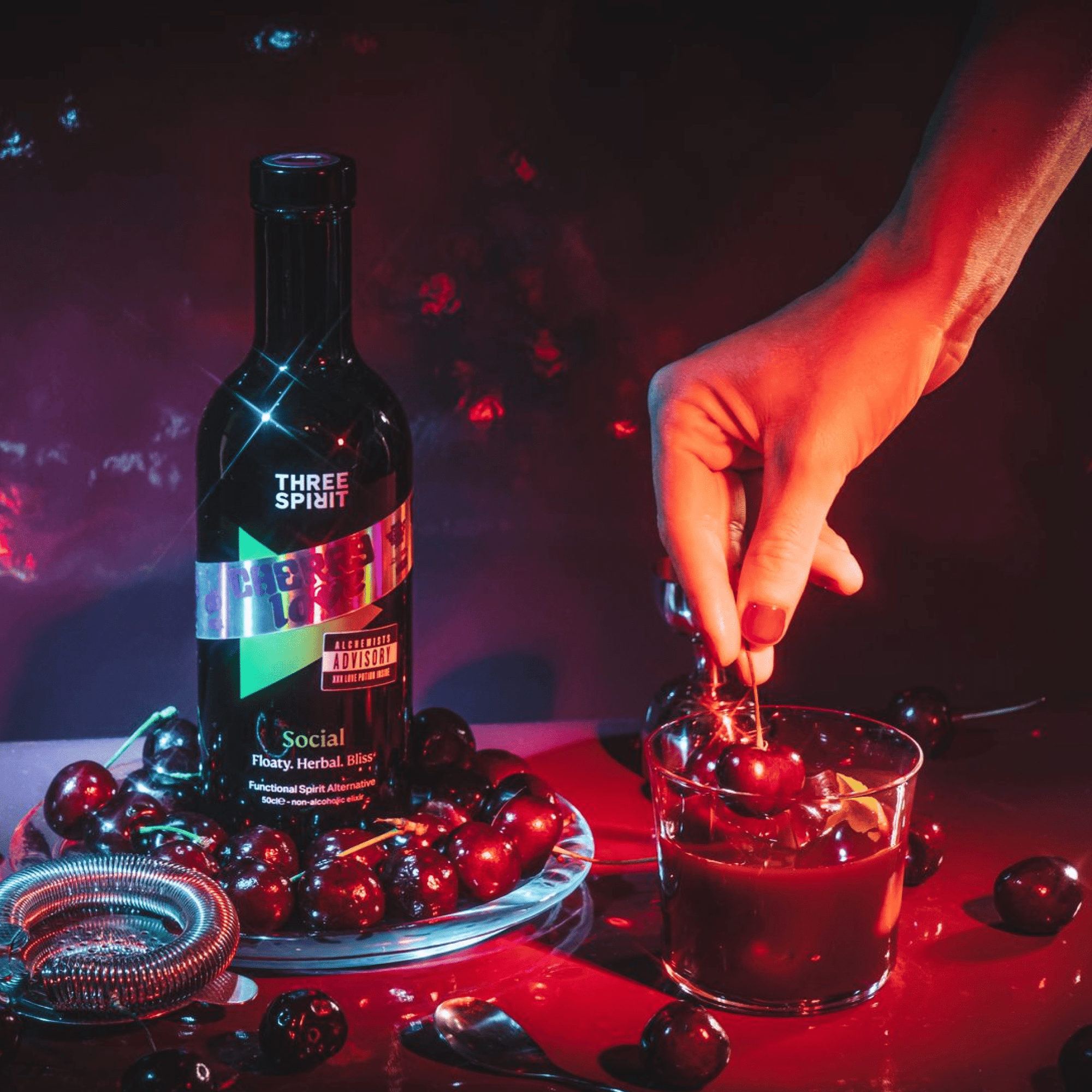 Bottle of Three Spirit Social liquor with a hand stirring a cocktail on a dark background